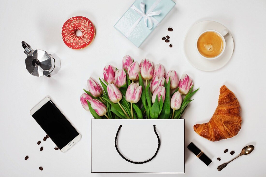 Stillleben mit Tulpen, Kaffee, Handy, Croissant, Donut, Geschenk und Kosmetika (Aufsicht)