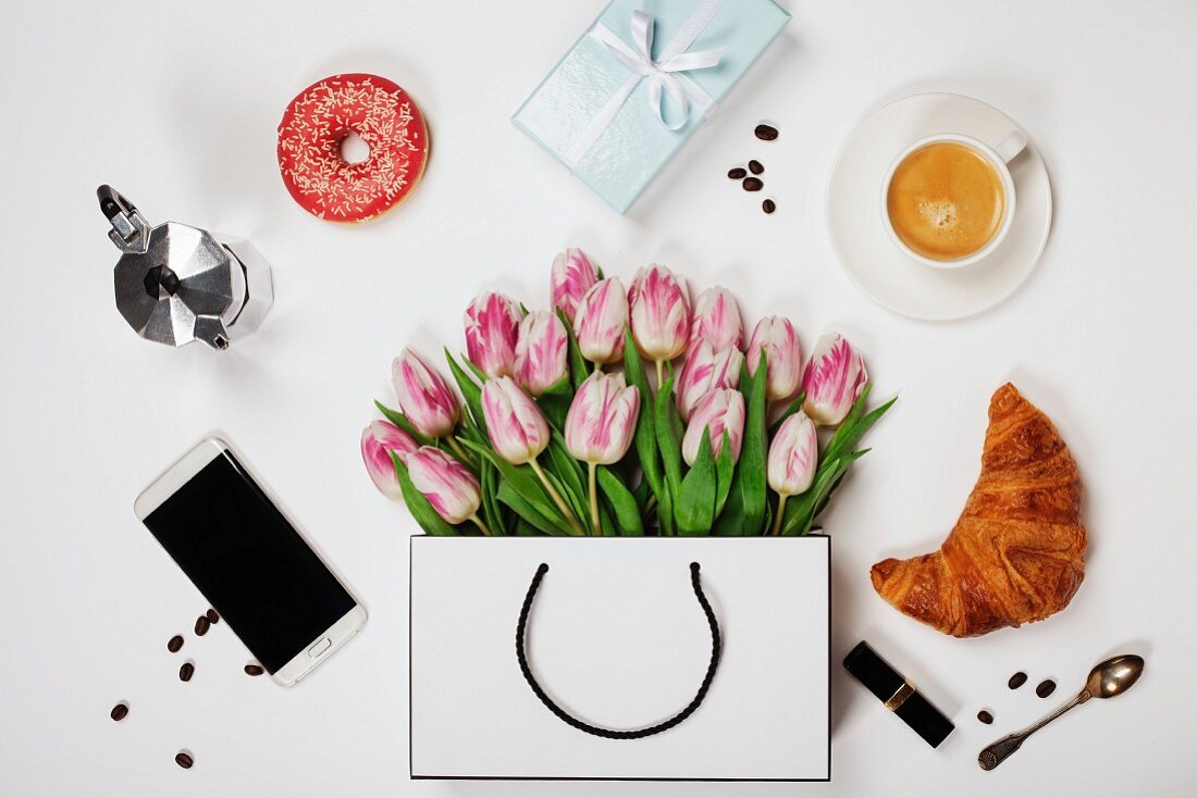 Top view of spring flowers, coffee, mobile phone, croissants, gift and cosmetics