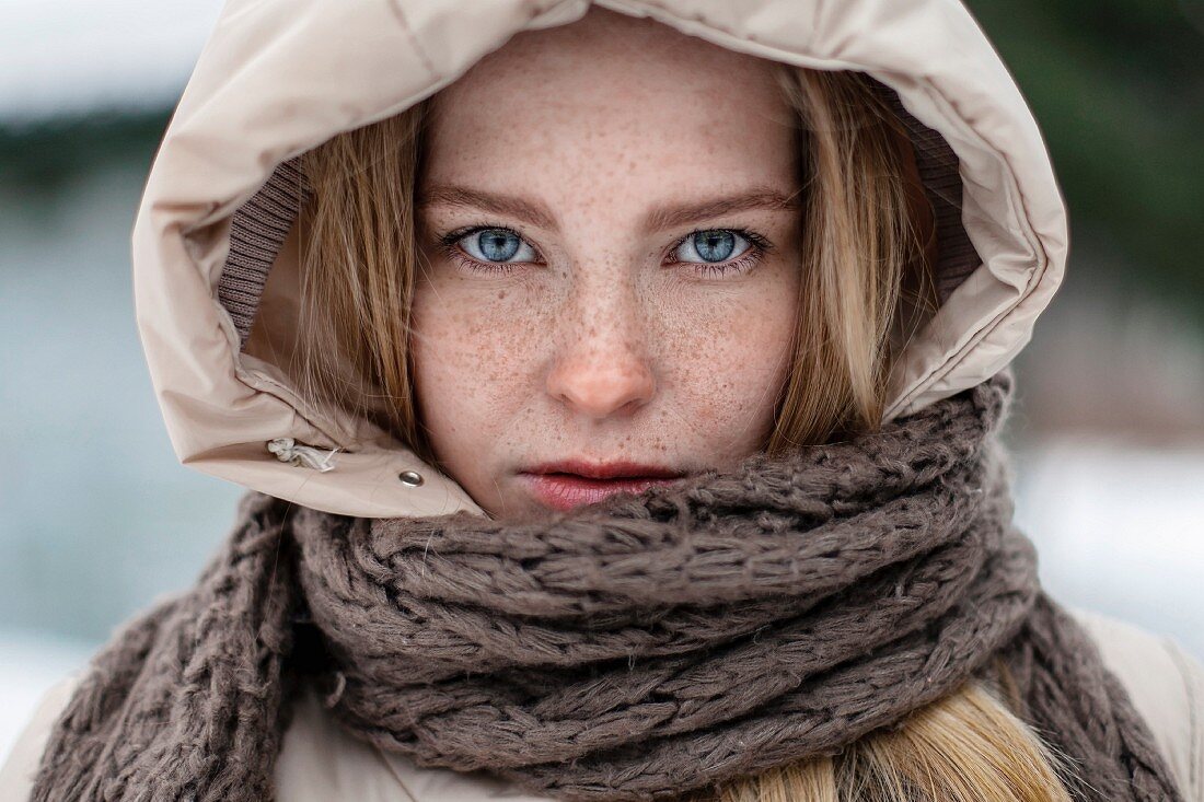 A red-haired woman with freckles wearing a hood and scarf