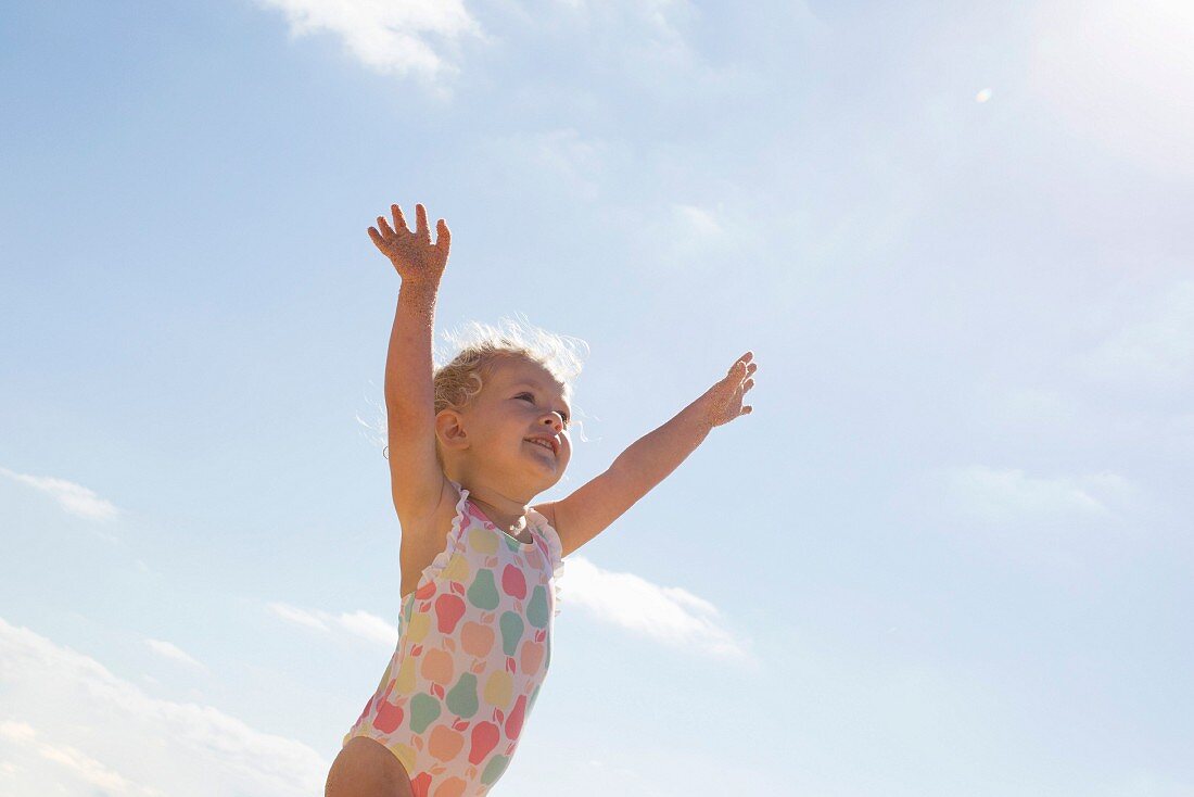 Kleines Mädchen im Badeanzug unter blauem Himmel