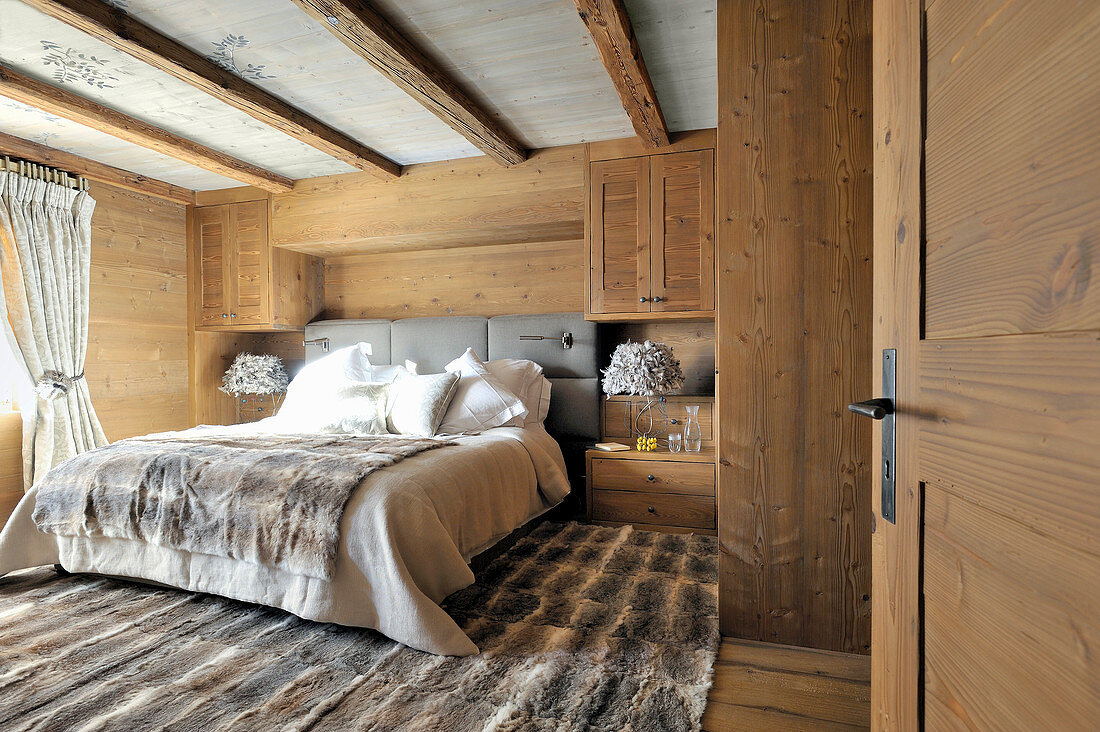 Fur rug and wood-clad walls in rustic bedroom