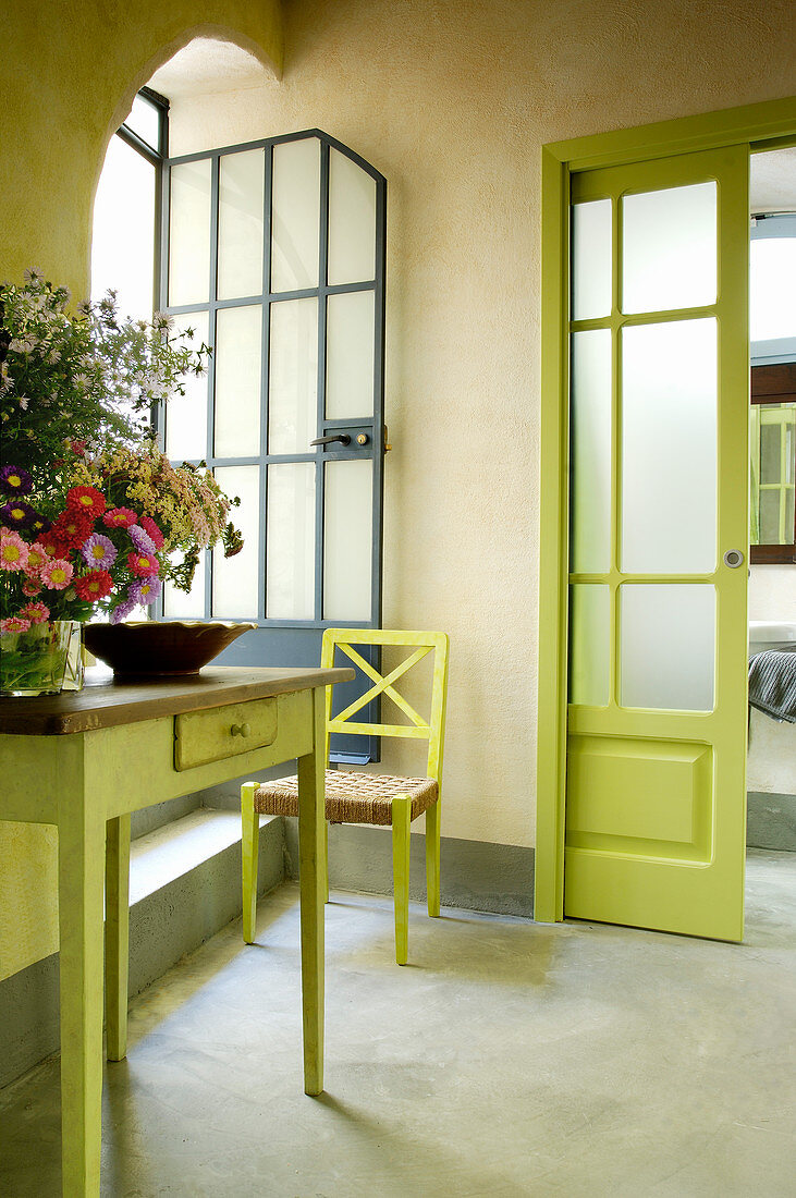 Knalliges Grün an Schiebetür, Stuhl und altem Tisch mit Blumen