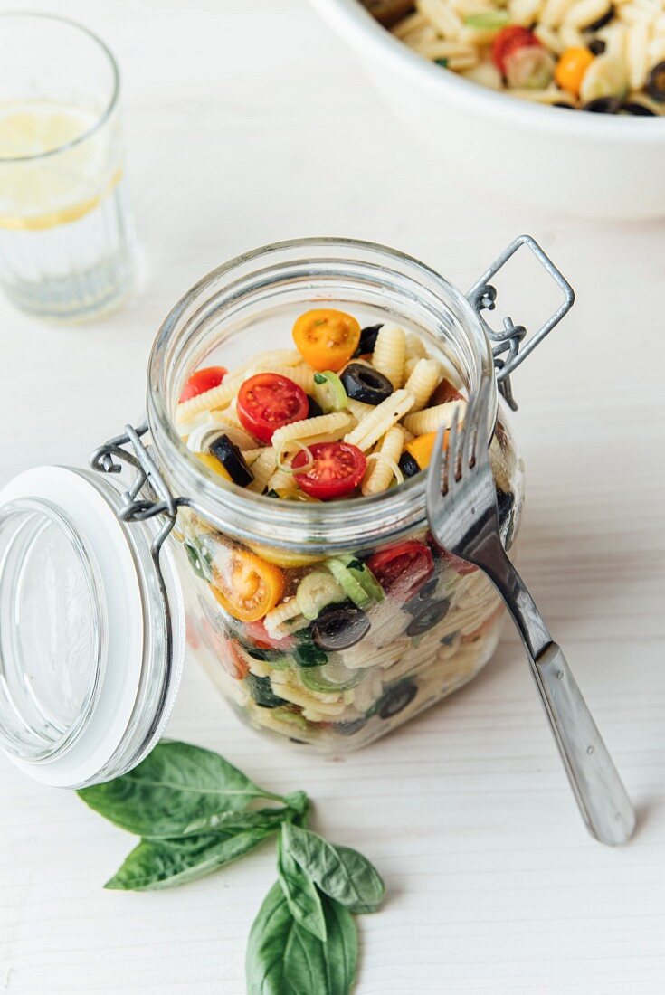 Mediterraner veganer Nudelsalat im Glas mit Kirschtomaten, Frühlingszwiebeln, Basilikum und Oliven