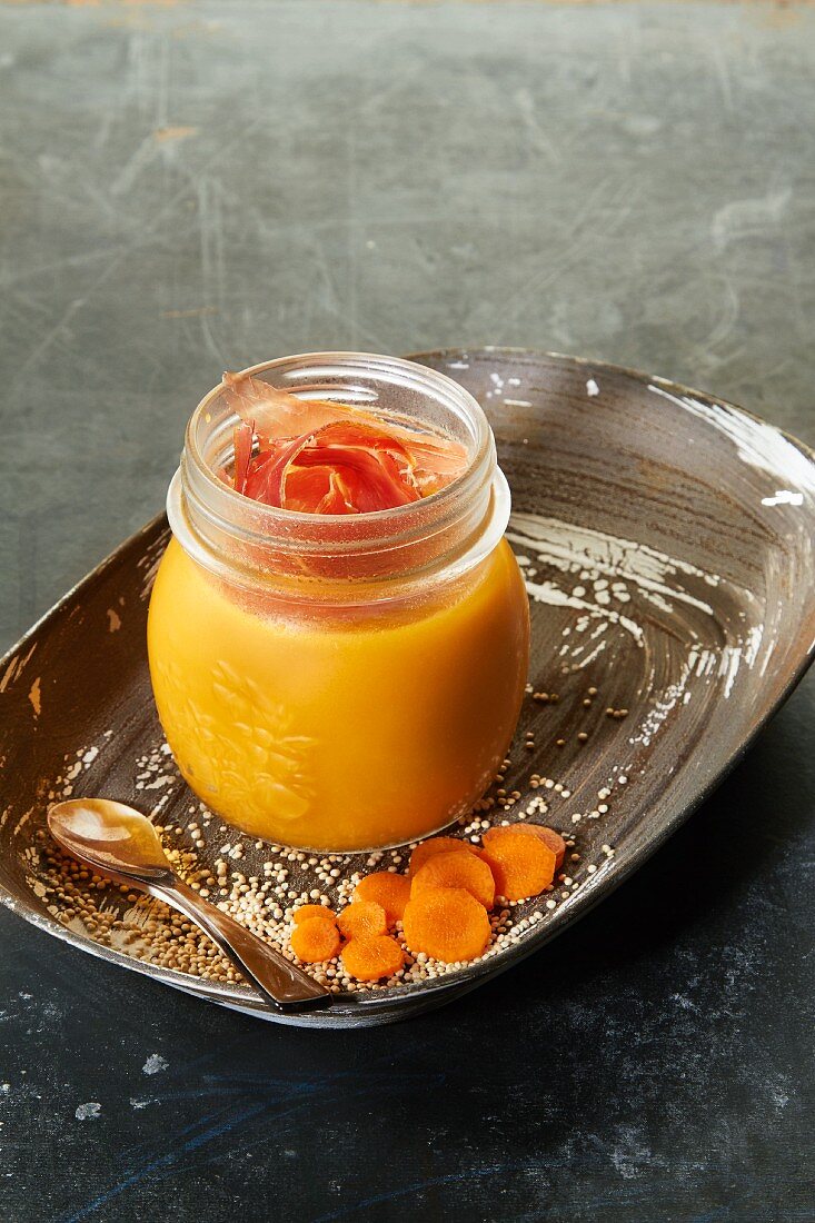 Creamy carrot and quinoa soup with raw ham in a glass jar