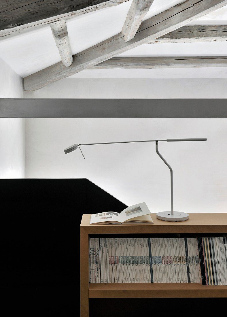 Designer desk lamp on magazine shelves next to black solid balustrade in loft apartment