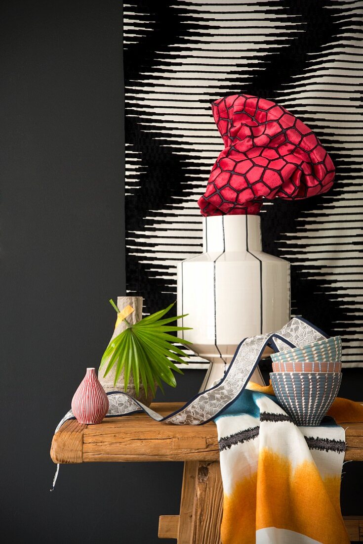 Stillleben mit Vasen und Schüsseln auf Holztisch vor schwarz-weisser Wanddekoration