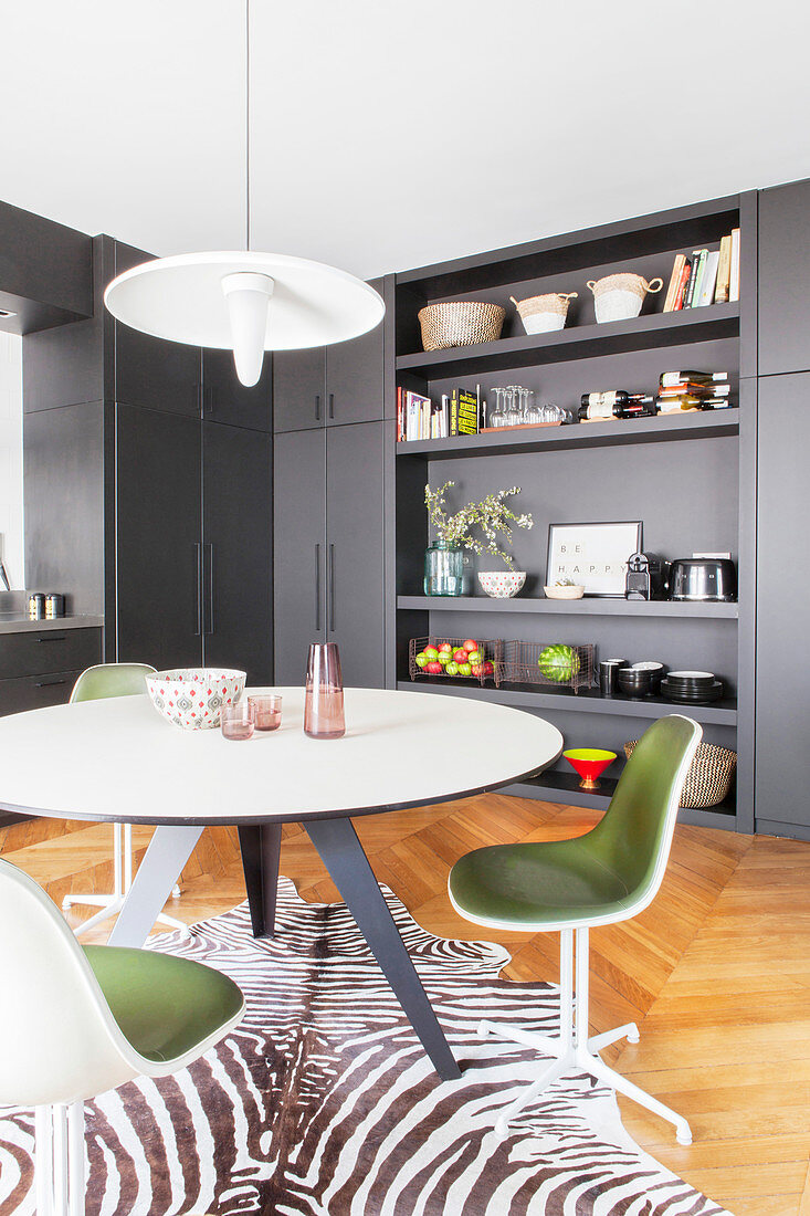 Round dining table and retro chairs on zebra-skin rug in grey fitted kitchen