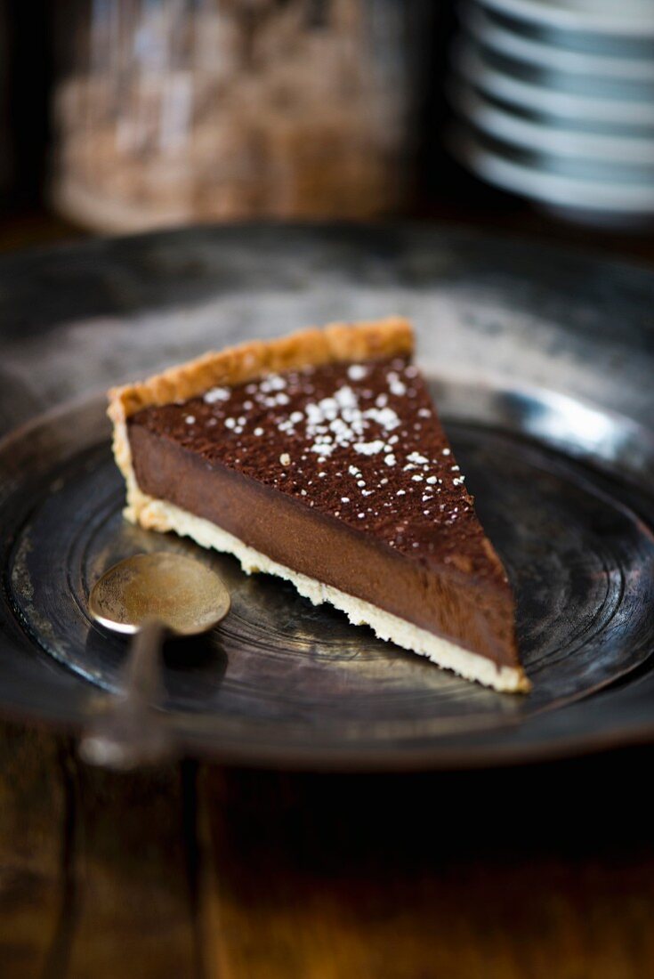 A piece of dark chocolate tart on a pewter plate with an antique spoon (France)
