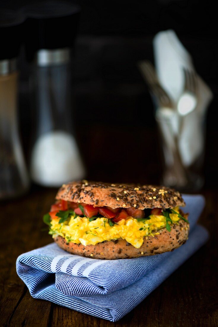 A corn bagel with egg and cress with mayonnaise, rocket and tomato