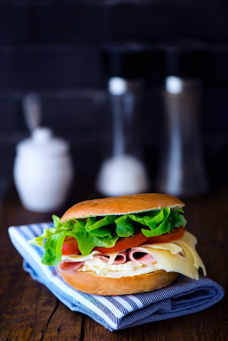 A bagel with cream cheese, cooked ham, cheese, tomato and salad