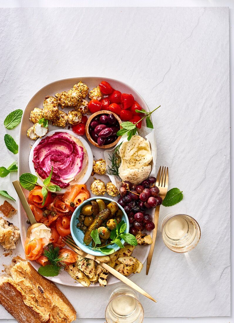 Lots of different antipasti on an oval platter with ciabatta and wine