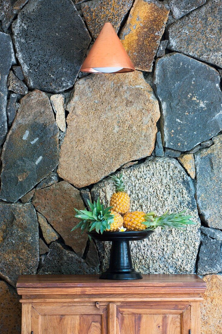 Dish of pineapples against rustic stone wall