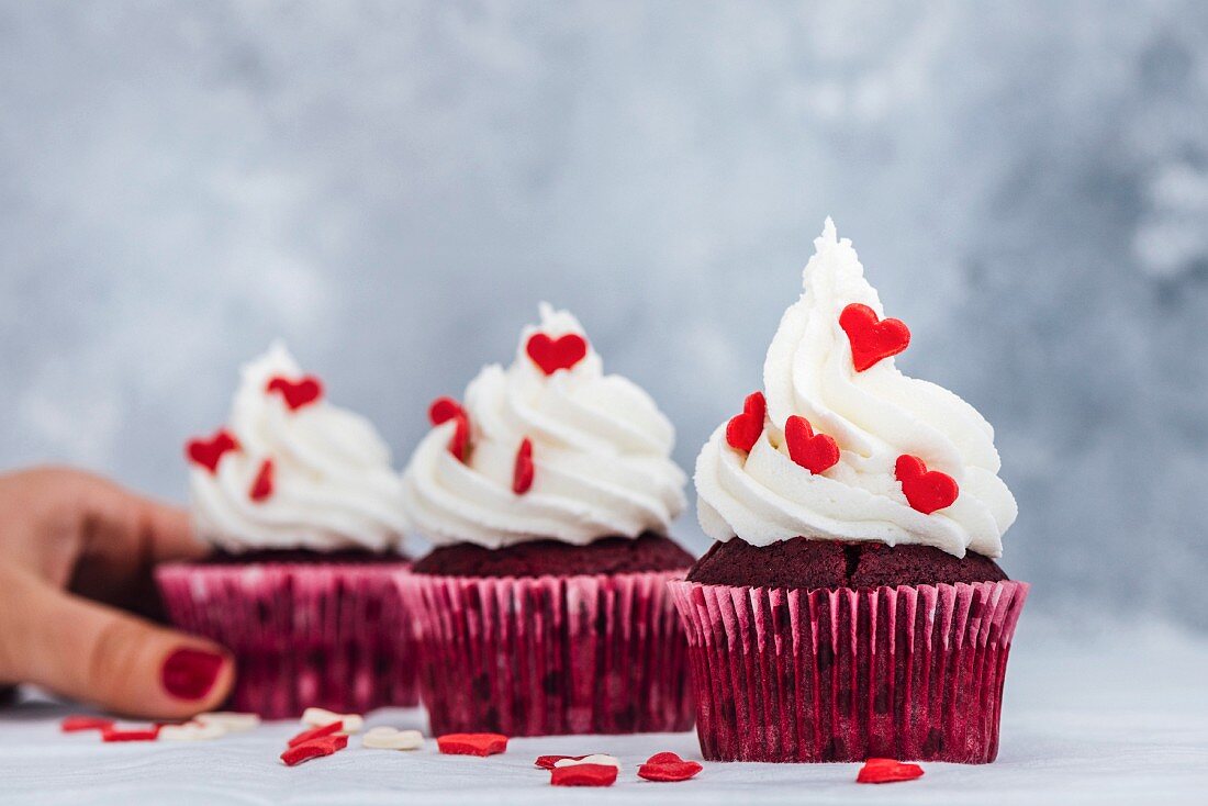 Red velvet cupcakes with buttercream frosting and decorated with heart shaped sprinkles