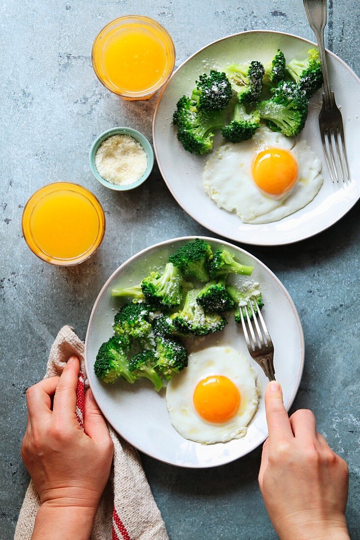Steamed broccoli with parmesan cheese, fried eggs and a glass of orange juice for breakfast