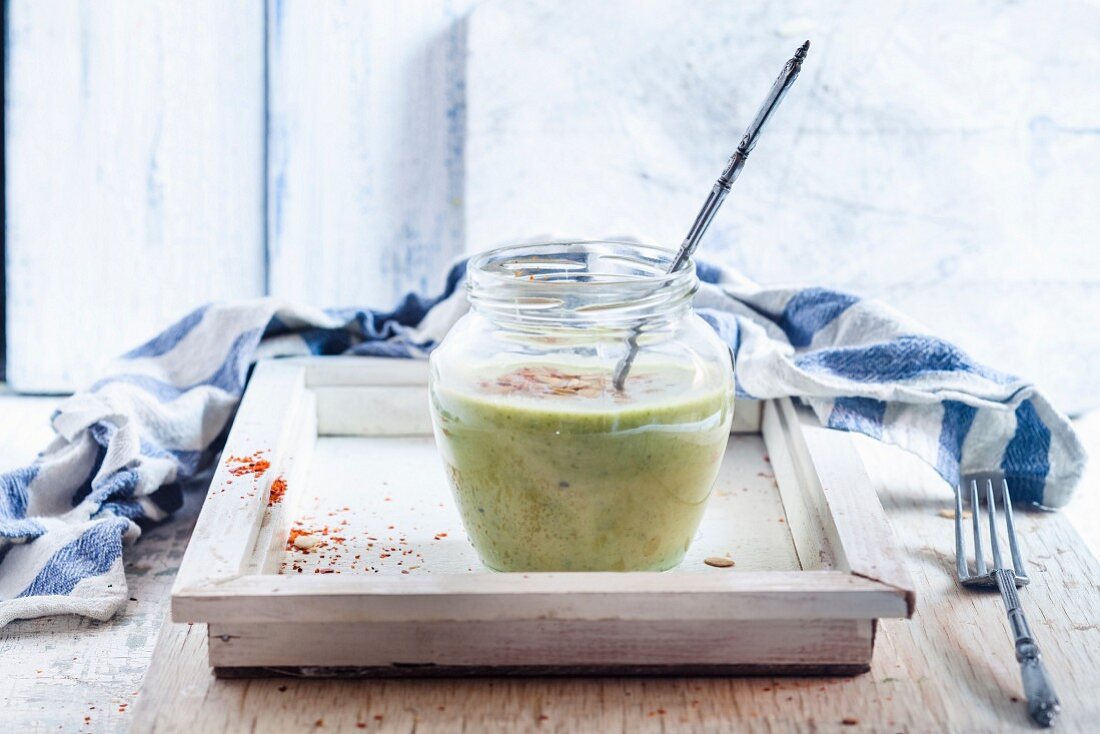 Spinach cream soup in a glass jar with roasted almonds and chilli flakes