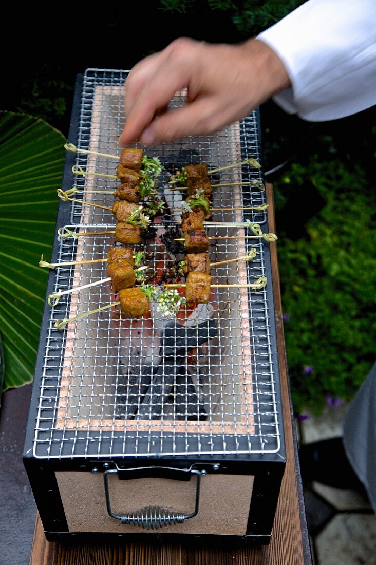 Koch grillt Hähnchenspiesse auf japanischem Konro-Holzkohlengrill mit Gitter