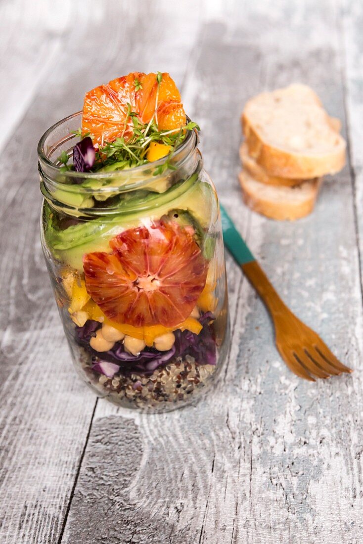 Quinoa salad in a glass jar with red cabbage, chickpeas, avocado, blood orange and cress