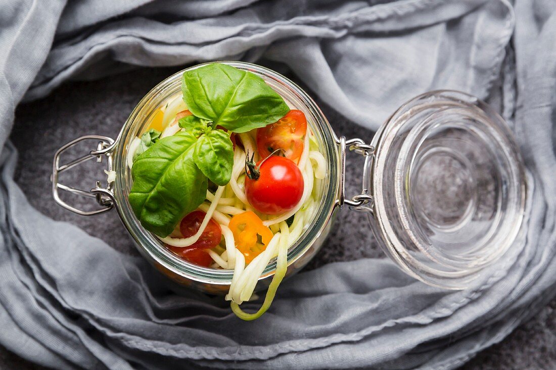 Zoodles (Zucchinispaghetti) im Glas mit Tomaten und Basilikum