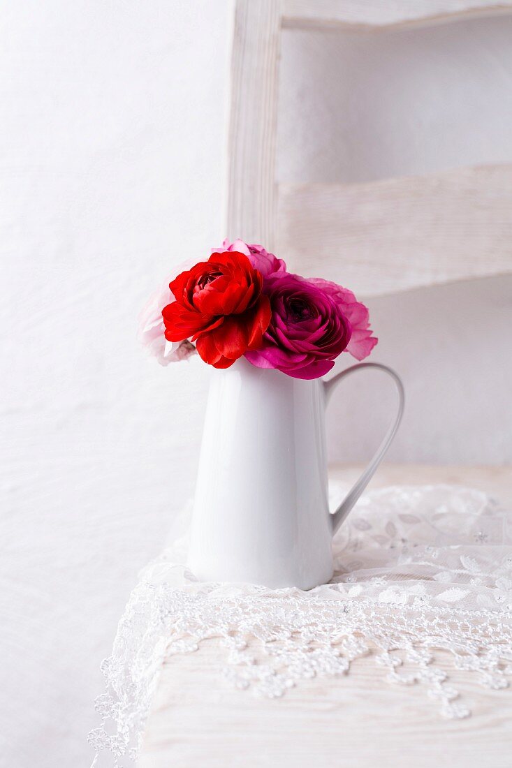Ranunculus in jug on lace doily on chair