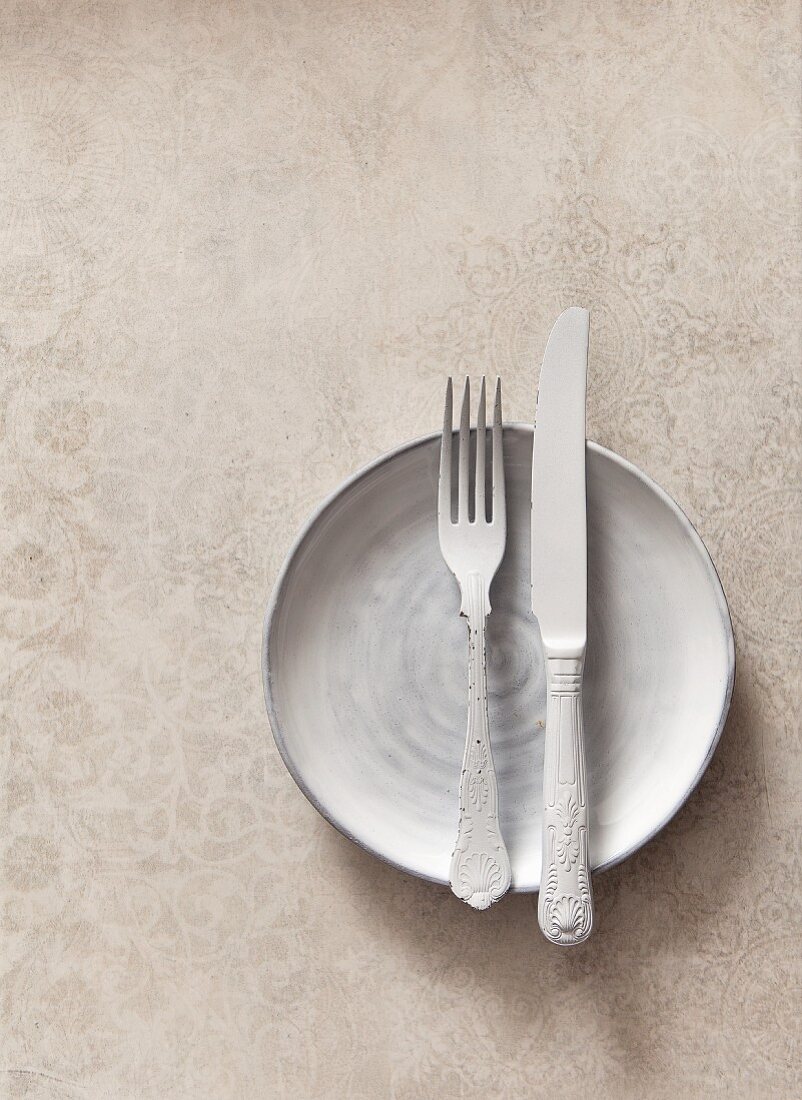 White cutlery on a white plate on a textured stone surface