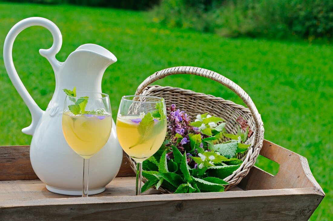 Apple juice with lemon and fresh herbs in glasses and a jug on a wooden tray