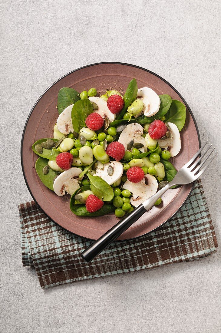 A mushroom salad with spinach, beans, peas and raspberries
