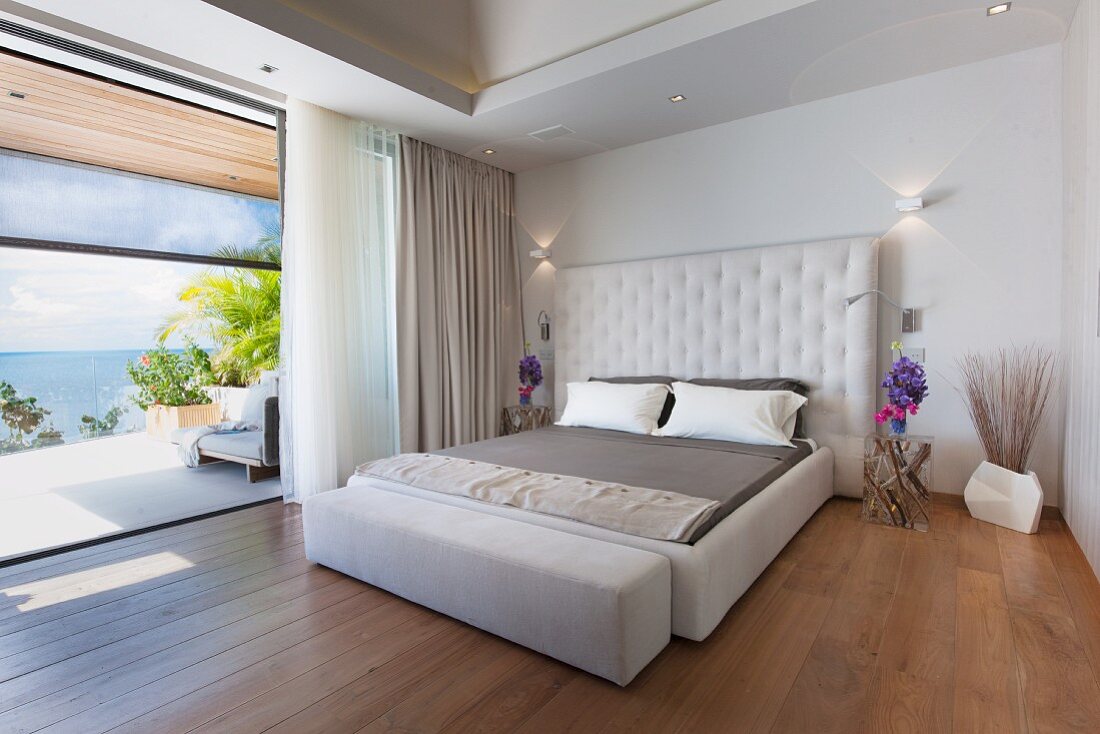 Upholstered bed and view of sea through panoramic window in bedroom