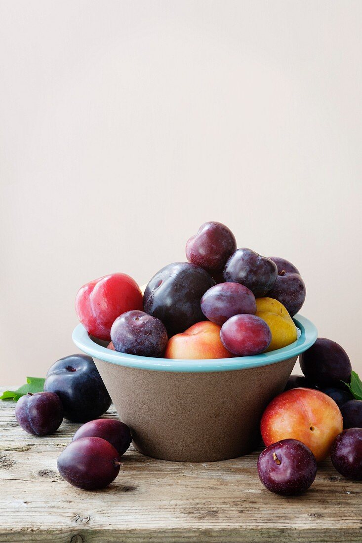 Plums in an earthenware bowl against a peach colour background