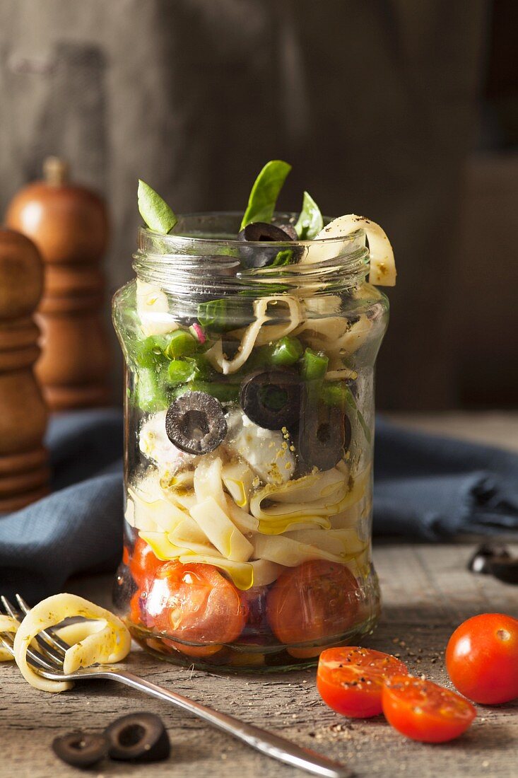 Italian style pasta salad in a lunch jar being eaten with tagliatelle wrapped around a folk in a rustic setting