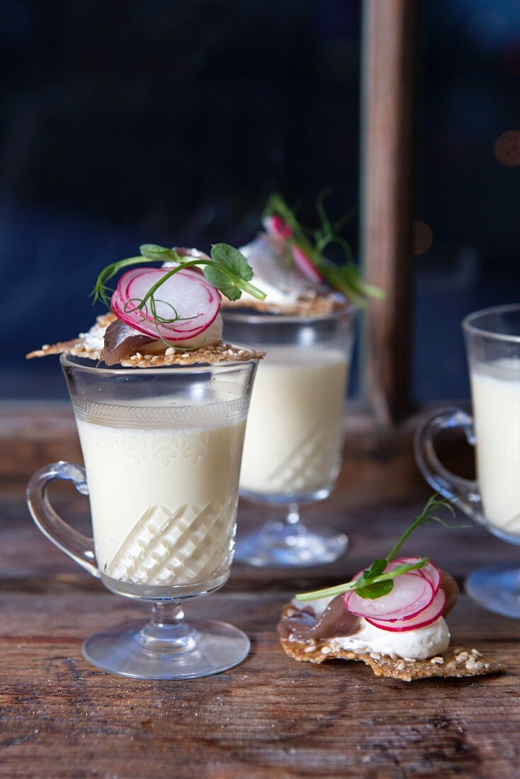 Cauliflower cream soup in glasses with crackers topped with herring cream cheese and radishes