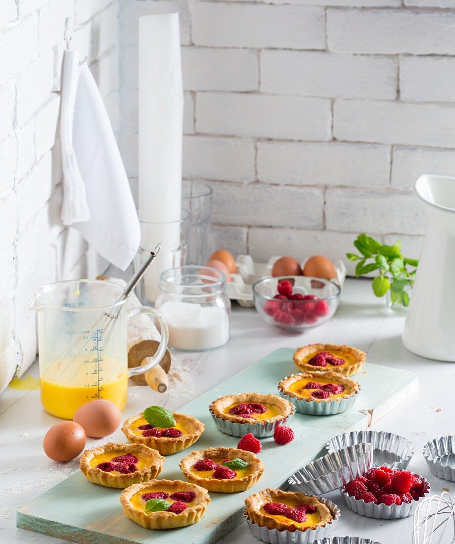 Raspberry and coconut tartlets with ingredients on a kitchen countertop