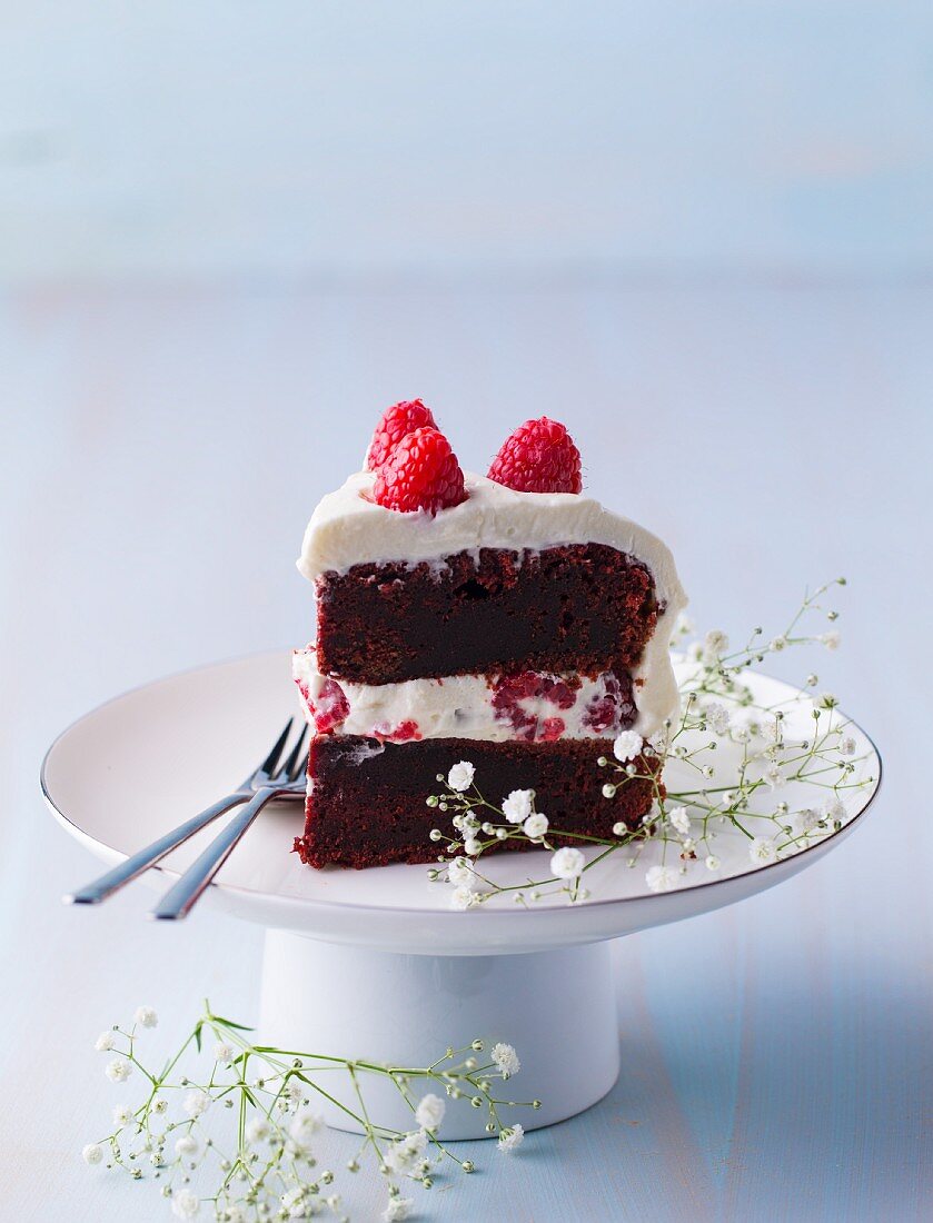 A piece of red velvet cake with raspberries on a cake stand