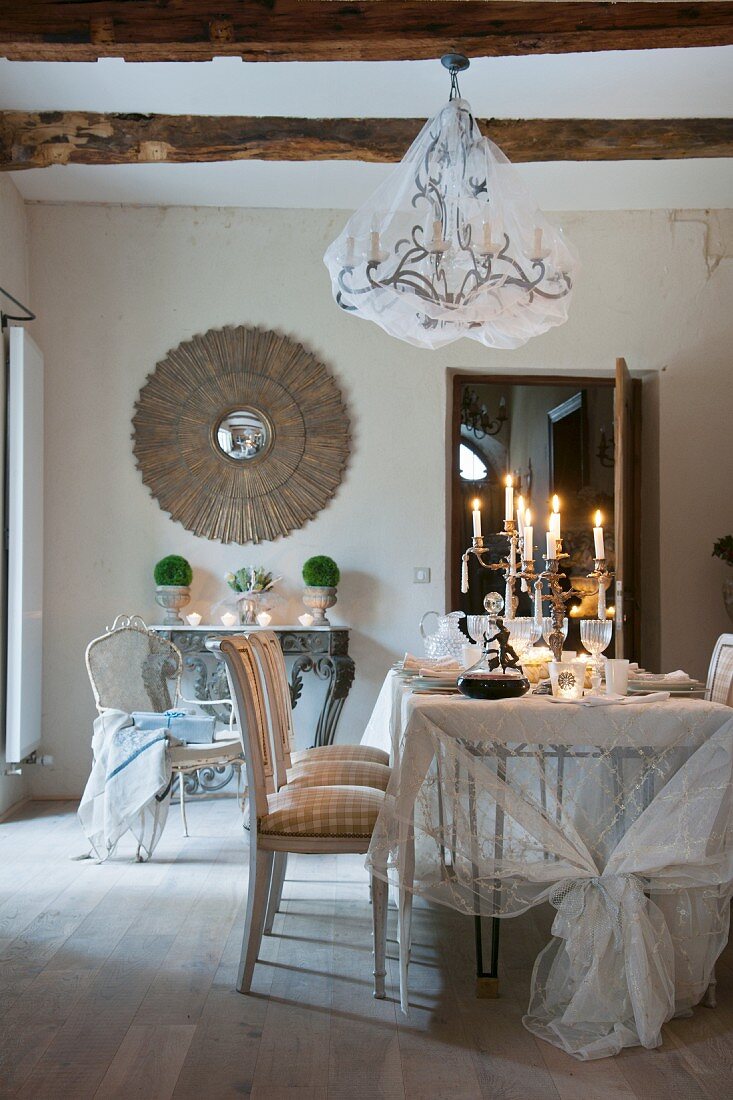 Chandelier with net cover above candles on festively set dining table in front of antique mirror on wall