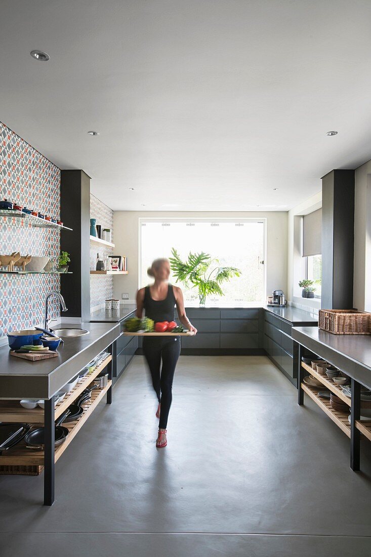 Woman carrying tray through large modern kitchen in shades of grey