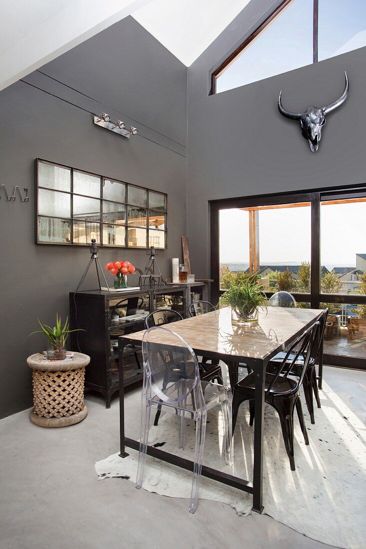 Long, industrial-style table and various chairs in high-ceilinged dining room with dark grey walls