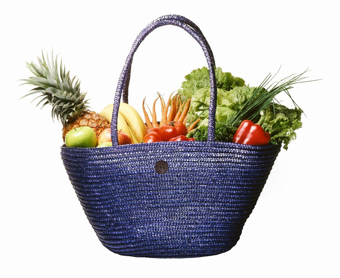 Korbtasche mit frischem Obst und Gemüse vor weißem Hintergrund