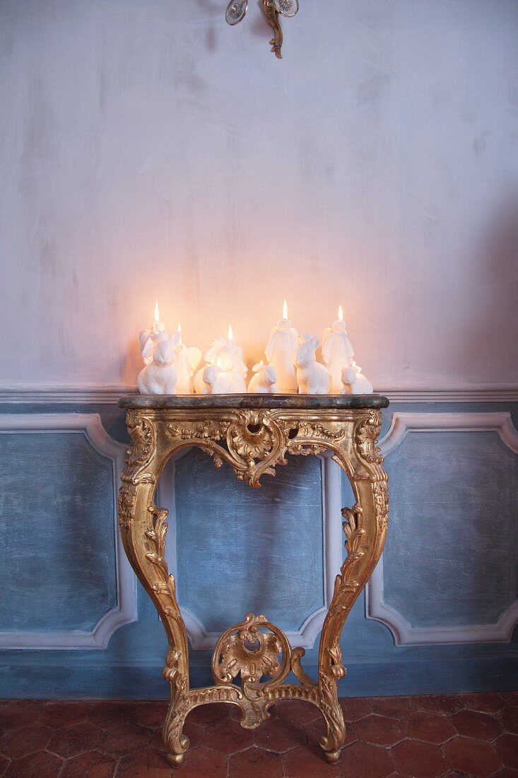weiße Kerzendekoration mit verschiedenen Motiven auf antikem, vergoldetem Konsolentisch