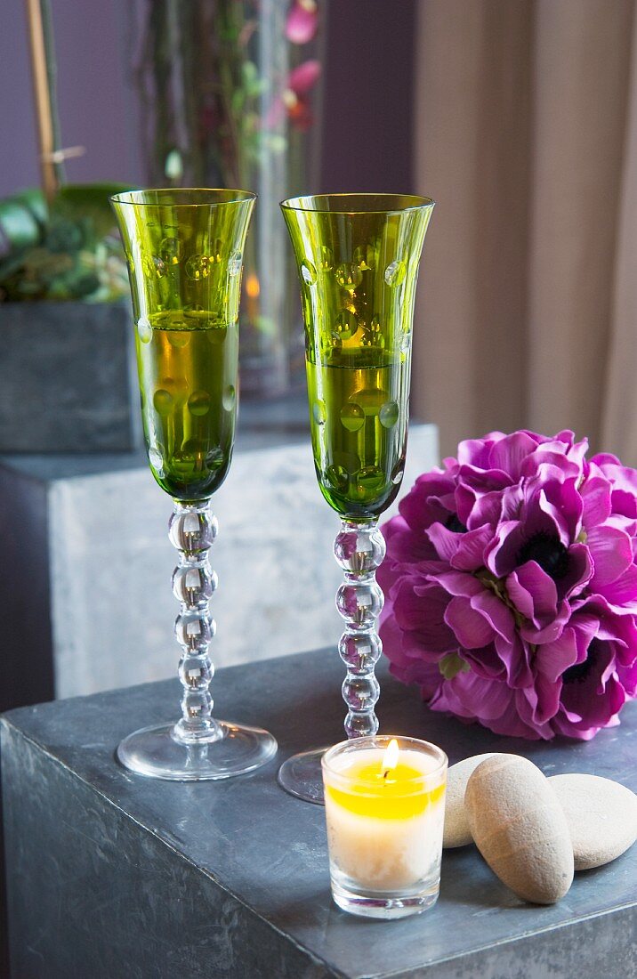 Grüne, elegante Sektgläser neben violetter Dekoblume und brennendem Teelicht