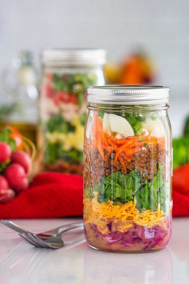 Layered salad in glass jars with spinach, carrots and cheese