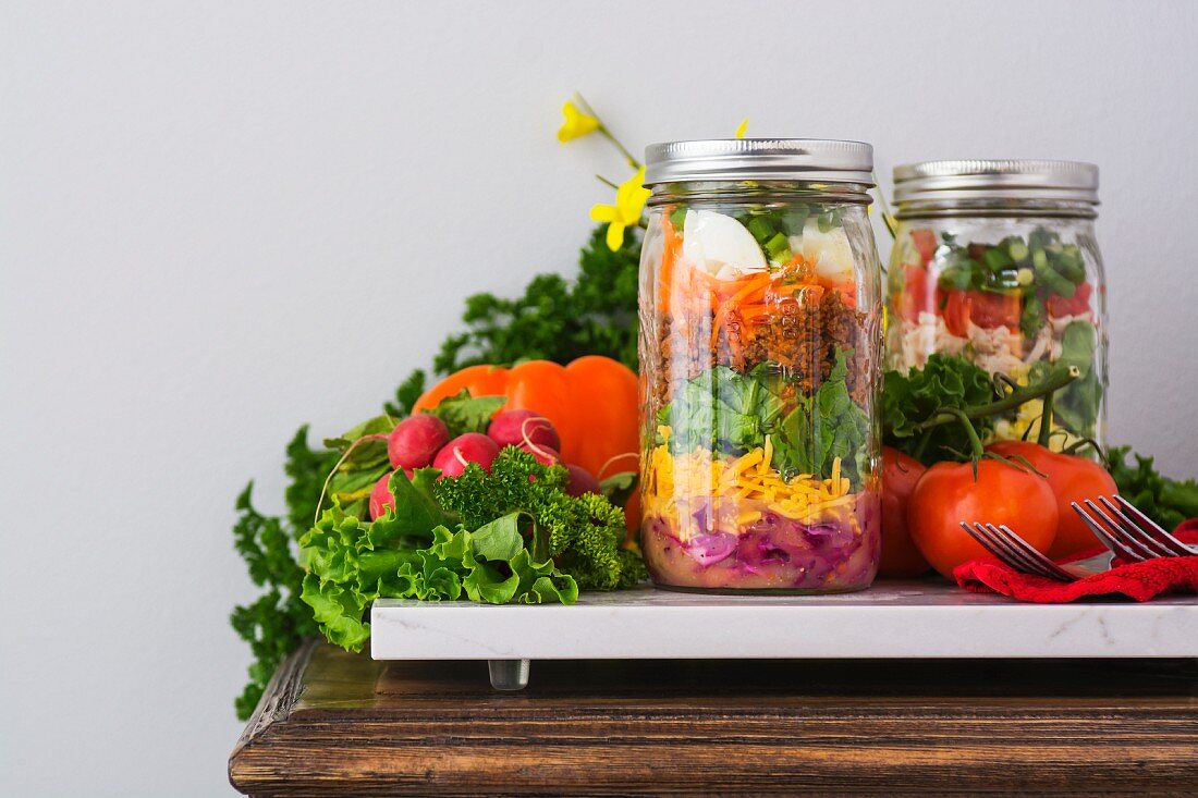 Two layered salads in glass jars with spinach, beans, cheese and eggs