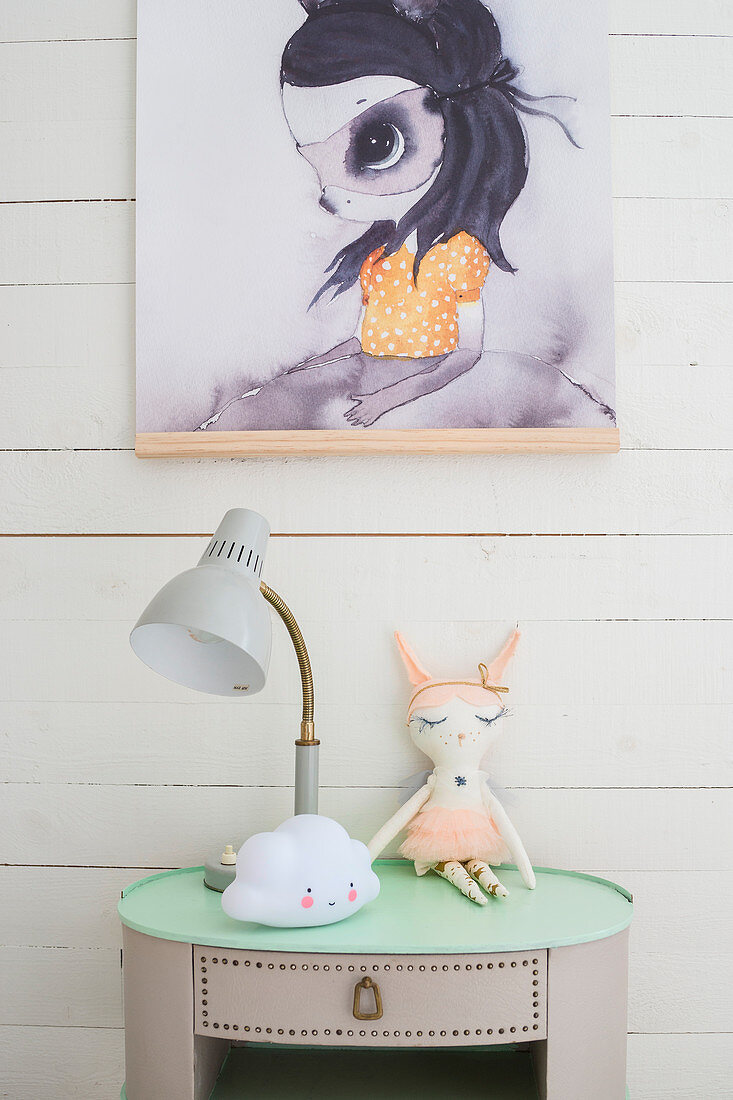Lamp and animal soft toy on vintage bedside table below poster on wall