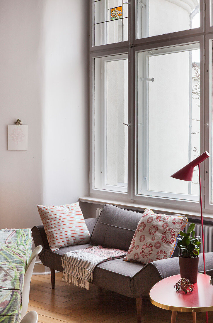 Sofa with scatter cushions, side table and standard lamp below window in period apartment