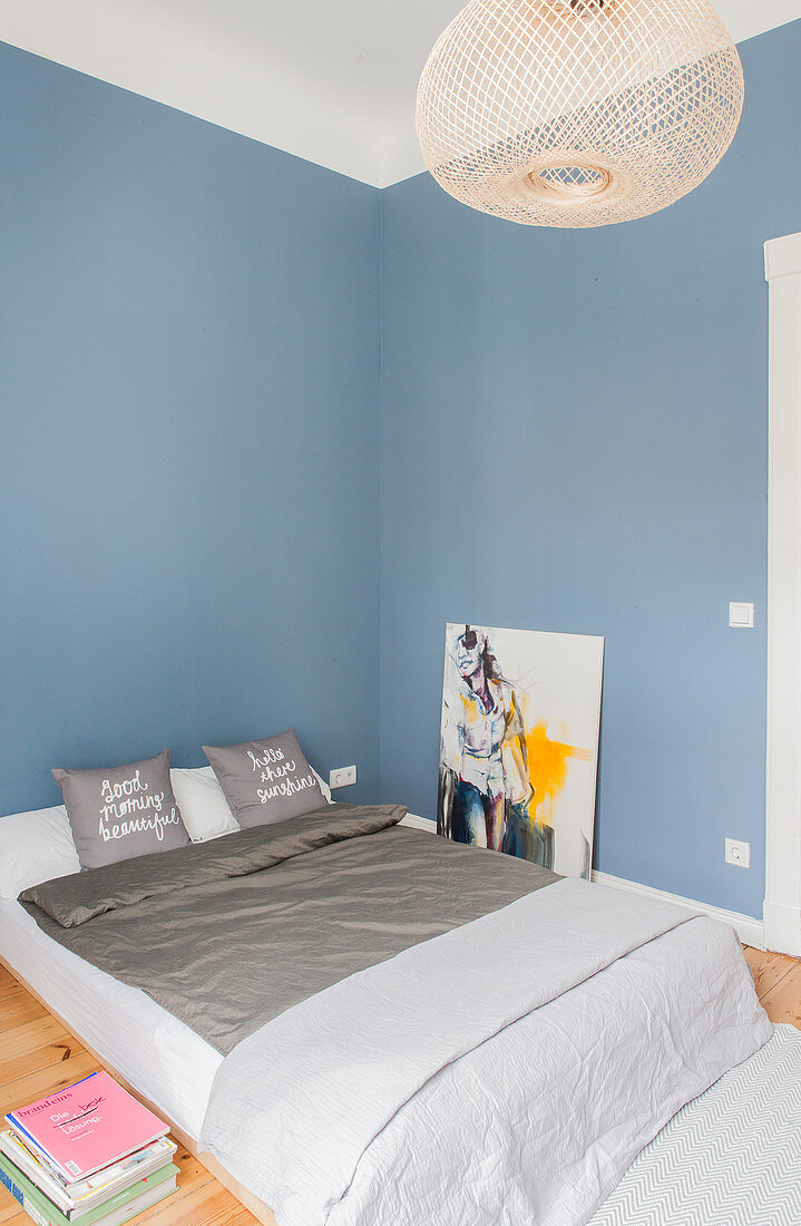 Doppelbett und moderne Kunst im Schlafzimmer mit blauer Wand