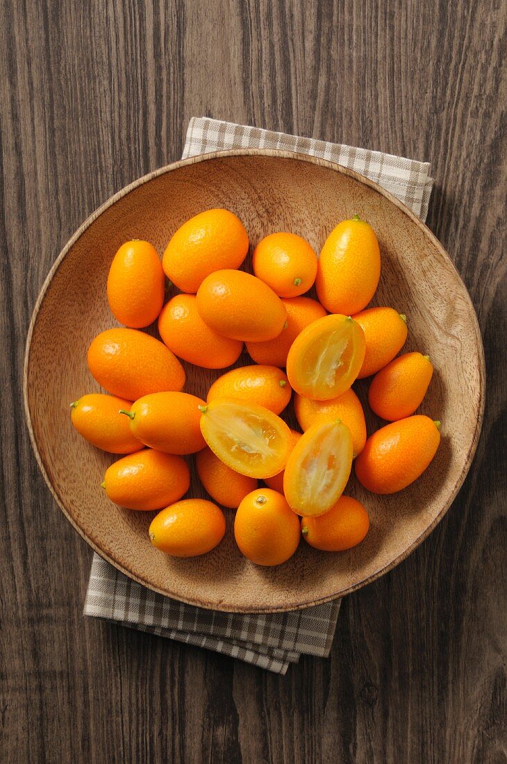 Fresh kumquats in a wooden bowl (top view)
