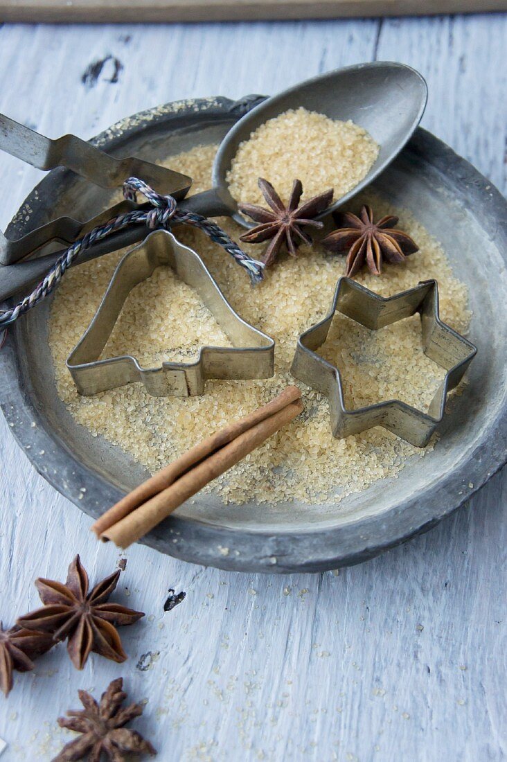 A plate with cookie cutters, a spoon, sugar, star anise and a cinnamon stick