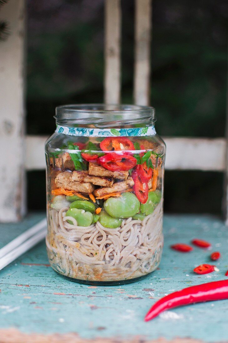 Miso soup in a glass jar with miso paste, soy noodles, beans, carrots, tofu, chilli and chopped spring onions