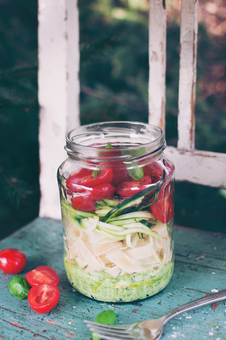 Tagliatelle with basil pesto, zucchini, cherry tomatoes and fresh basil in a glass jar