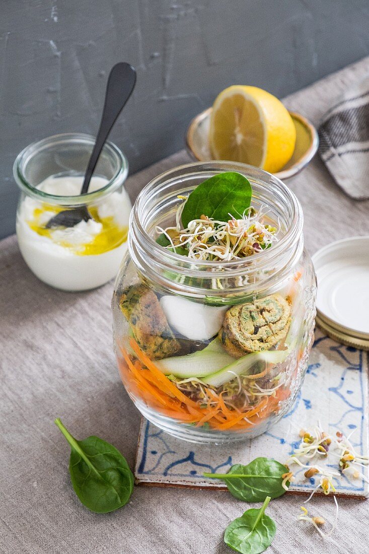 A vegetable salad with herb frittata rolls in a glass jar