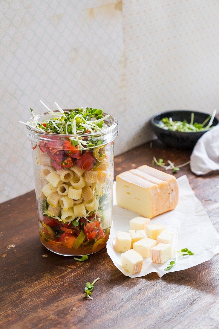 A pasta salad in a glass jar with tomatoes, olives and cheese
