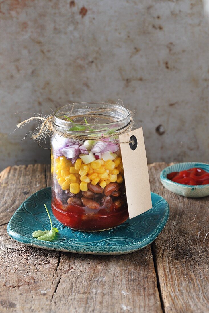 Layered salad with beans, corn and red onion in a glass